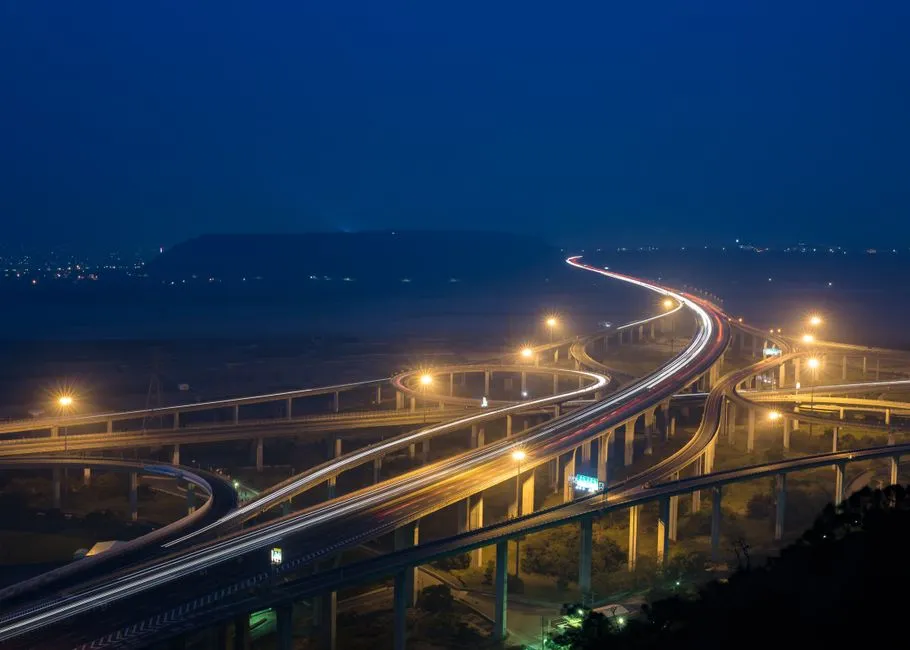 A highway interchange at night in long exposure, light trails tracing the lanes
