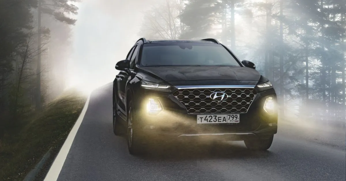 A modern SUV driving on a foggy forest road with headlights on, a degraded-visibility scene